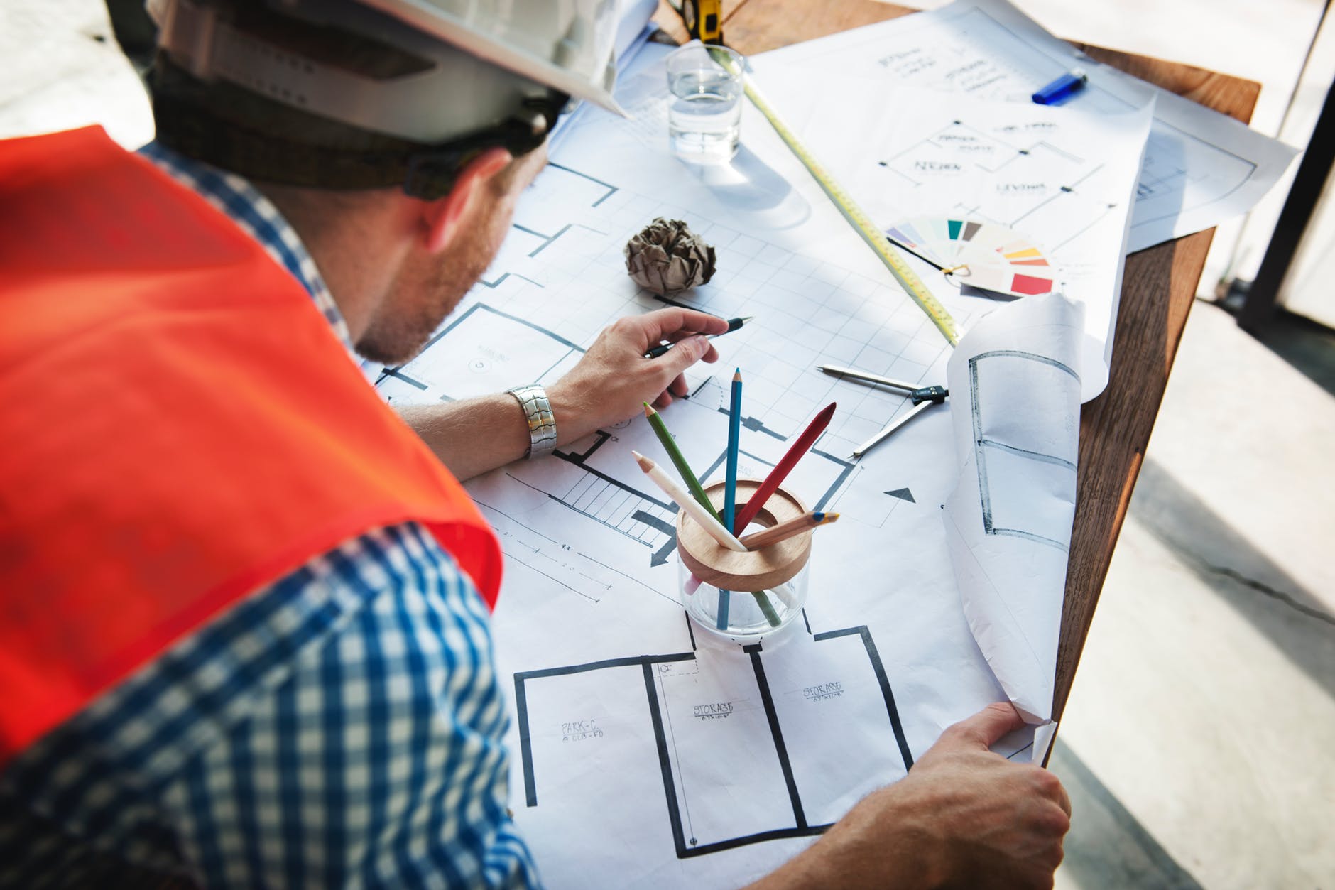 man wearing white hard hat leaning on table with sketch plans